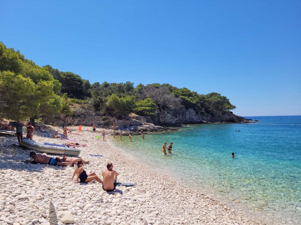 Srebrna white pebble beach near Vis town backed by pine trees with clear calm water on the Dalmatian Coast