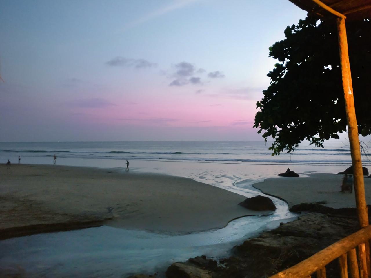 Crowds gathering on a wide west facing sand beach as the sun drops into the sea in Goa