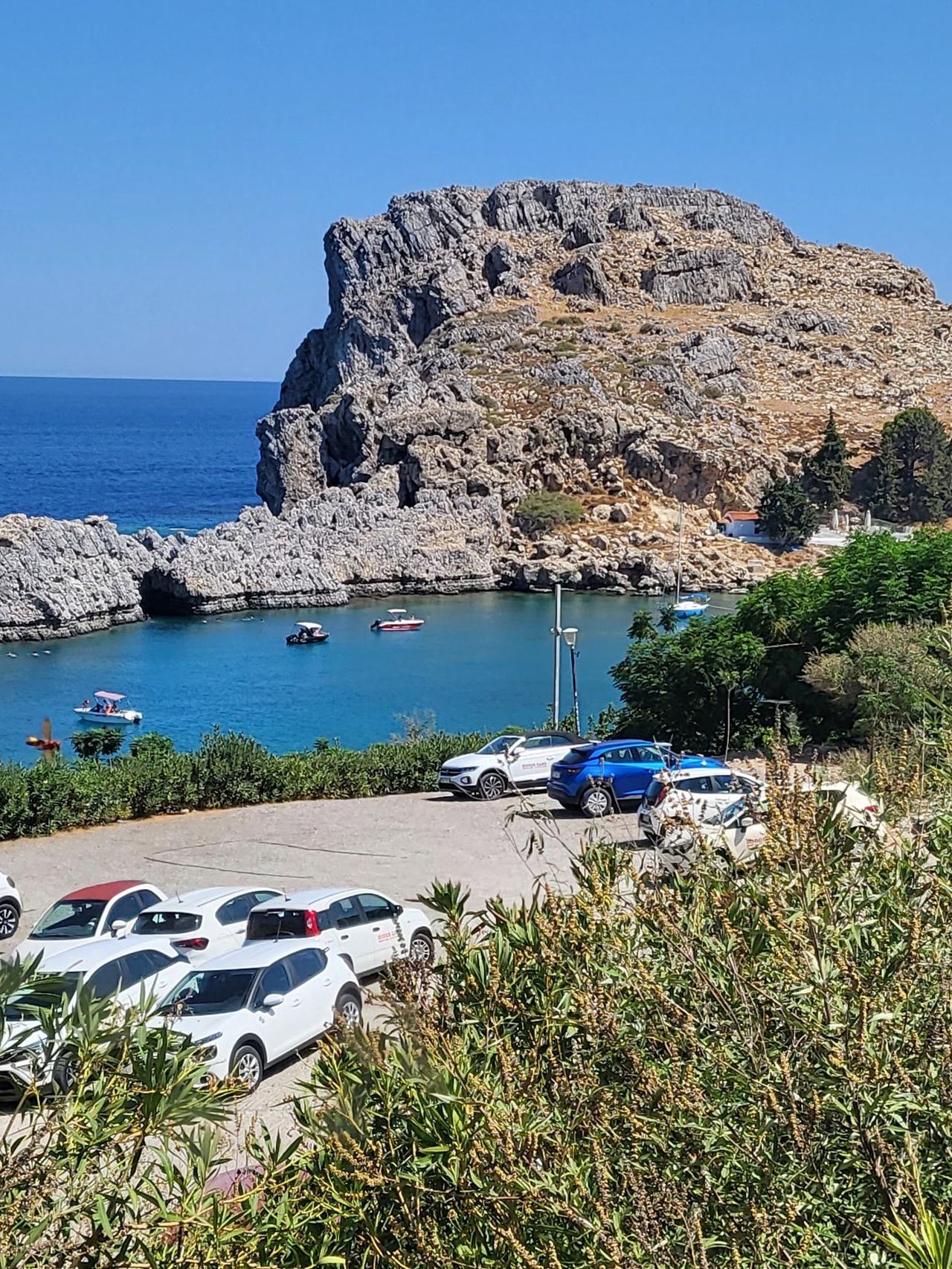 The narrow opening and clear sheltered water of St Pauls Bay with the small white chapel and Acropolis of Lindos on the cliffs above on Rhodes