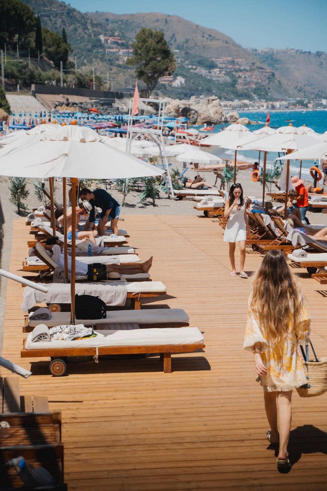 Sun loungers and terraces on the private sandy cove at Tao Beach Club near Taormina in Sicily