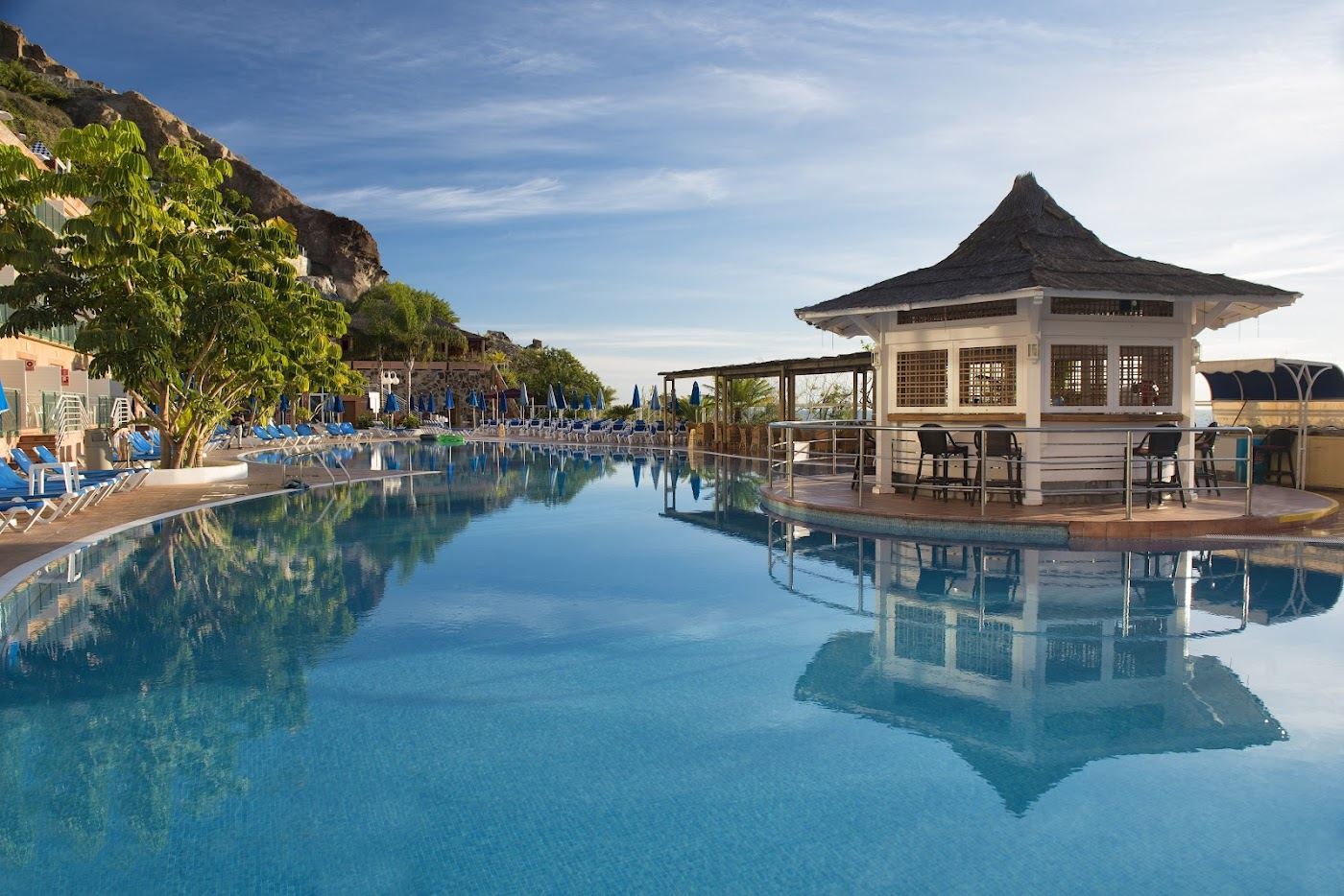 Dark sand beach backed by mountains and a pool complex at Taurito in south west Gran Canaria