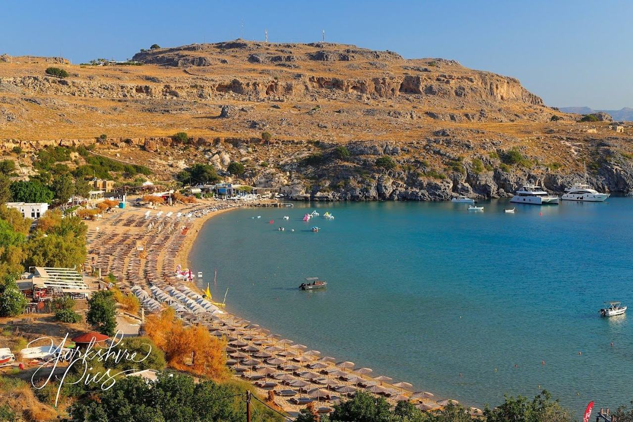 The sheltered bay below Lindos on Rhodes with clear warm water and a curve of sand